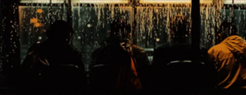 Silhouettes of passengers behind a window streaked with rain